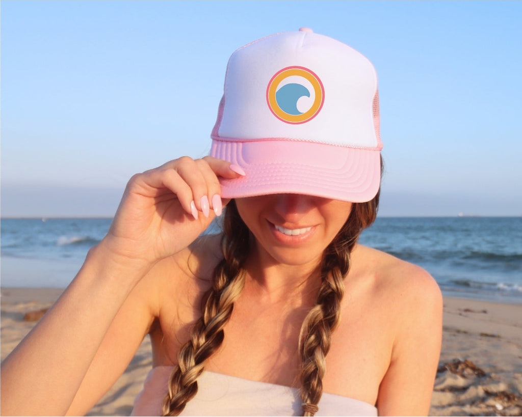 Person wearing a pink and white cap with a logo on a beach