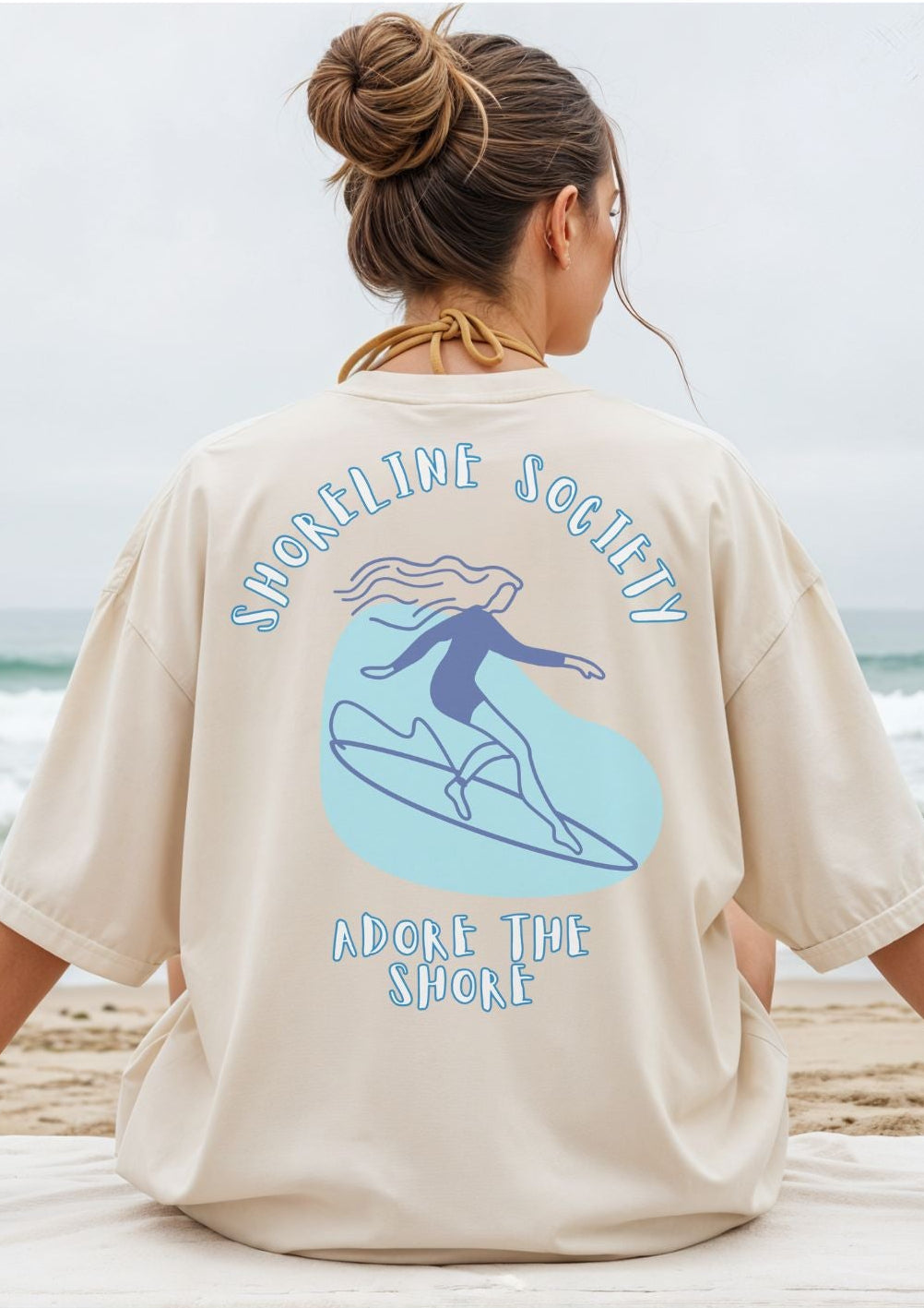 Person wearing a beige t-shirt with a graphic design on the beach