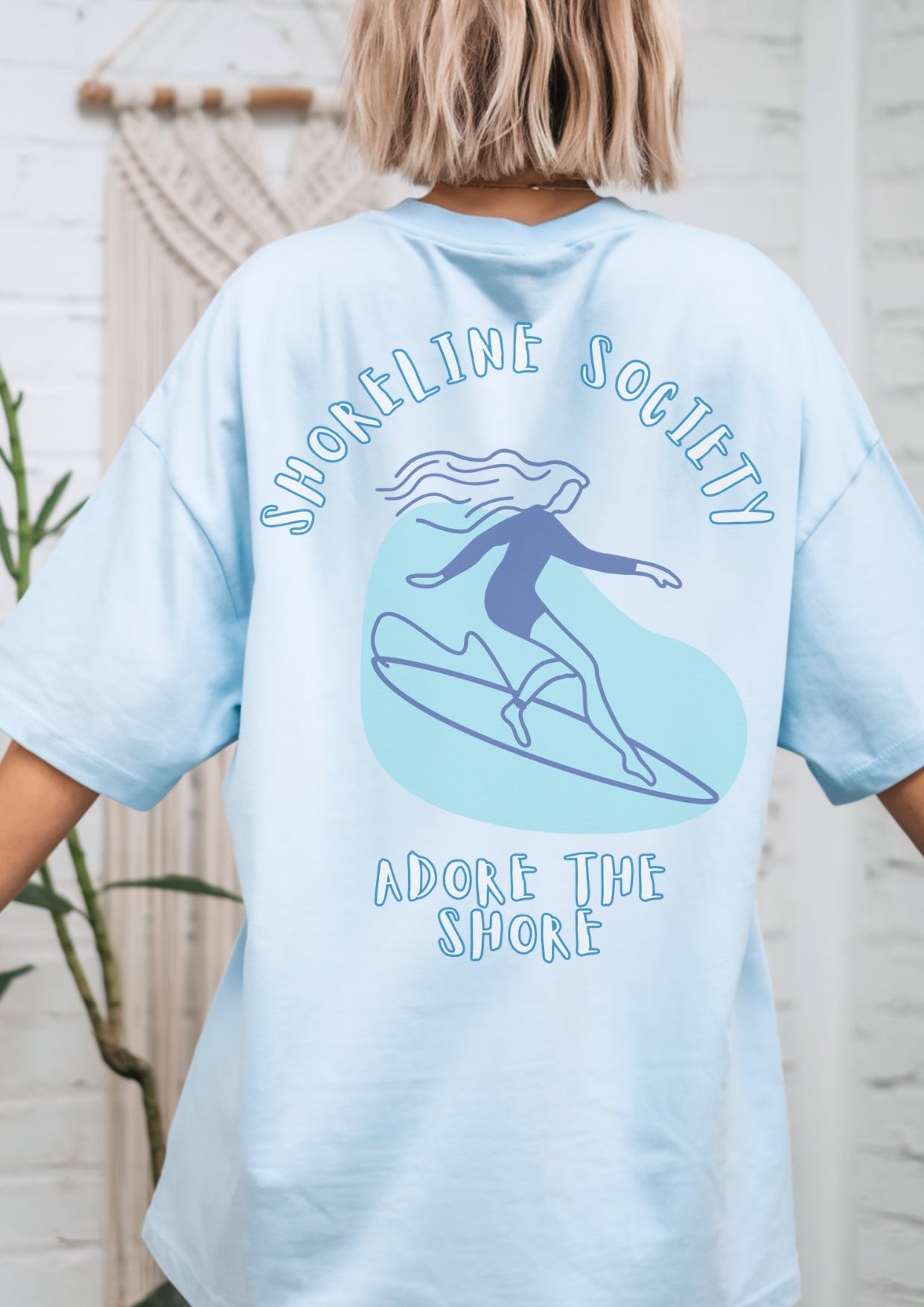 Light blue t-shirt with graphic design and text, worn by a person indoors.