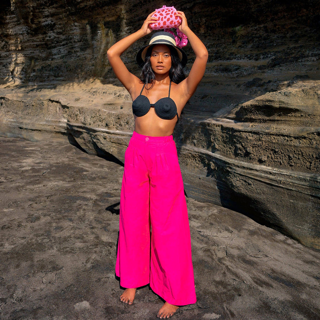 Person wearing a black bikini top and bright pink pants standing on rocky terrain.