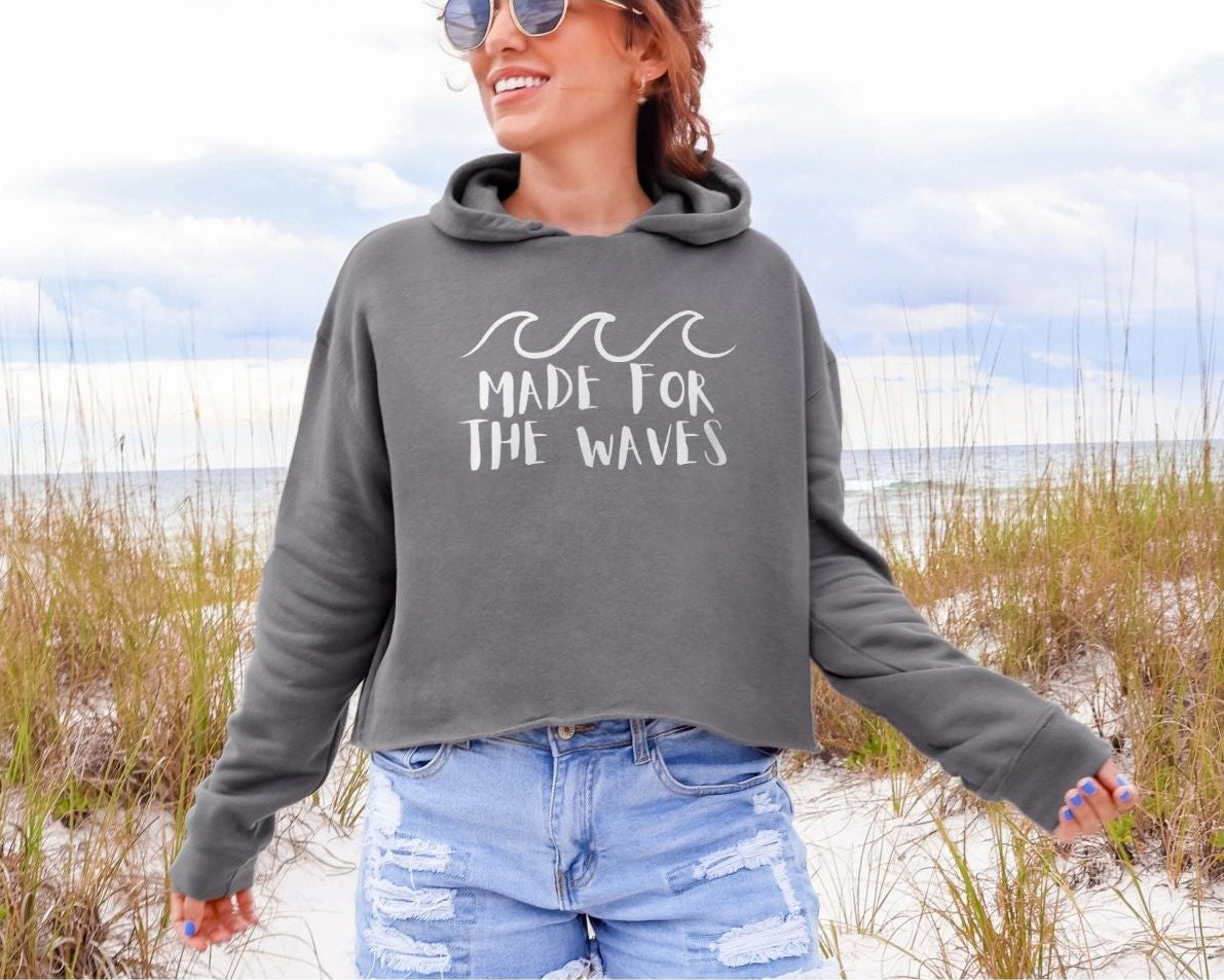 Woman wearing a hoodie with 'Made for the Waves' text on a beach